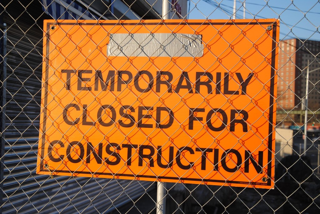 Sign attached to chain link fence that says closed for construction